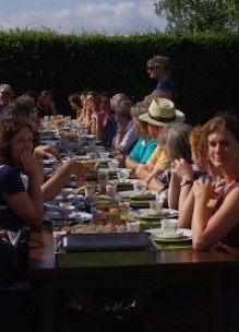Groep mensen geniet buiten in de boomgaard aan tafel van theeleut hightea met diverse huisgemaakte zoete en hartige lekkernijen in Udenhout