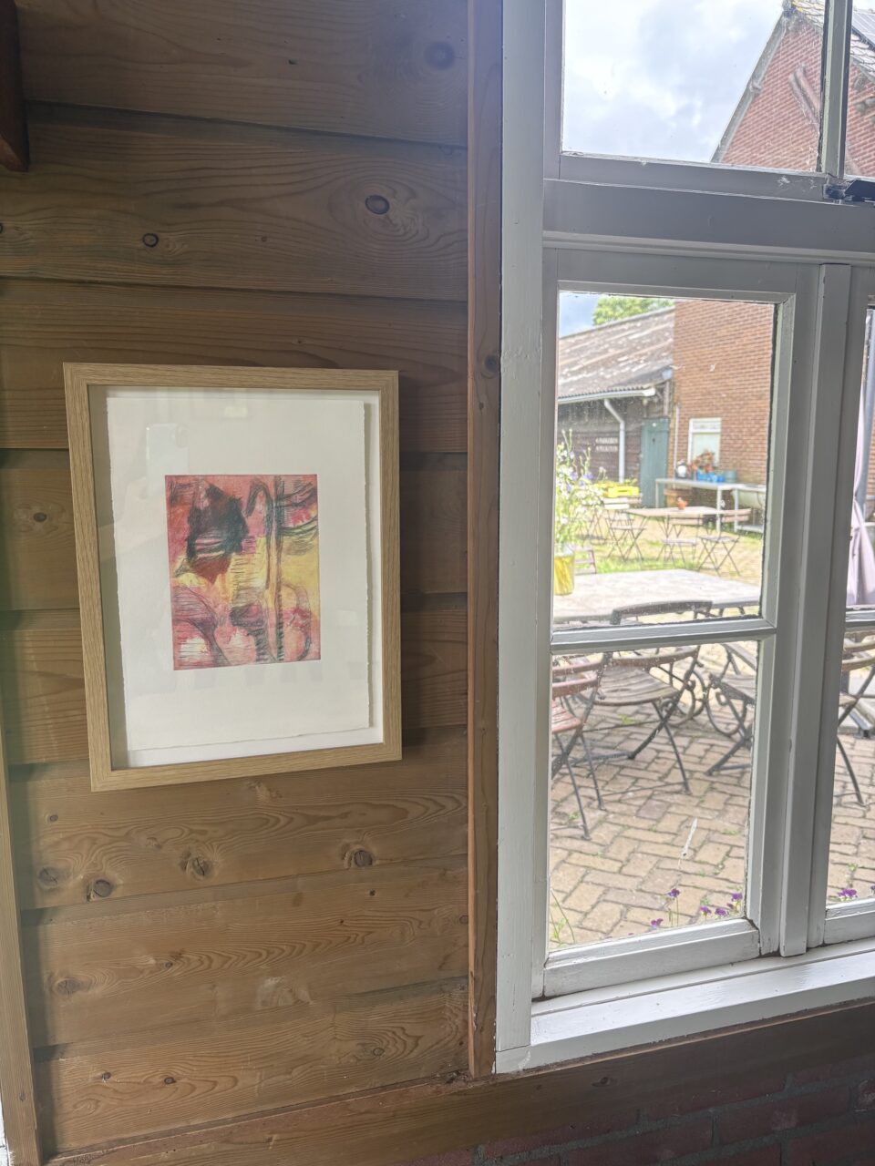 werkje in lijst aan de muur met doorkijkje door raam naar terras van Sprankenhof
